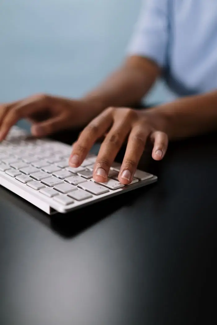 A close-up view of hands typing on a sleek white wireless keyboard on a desk.
