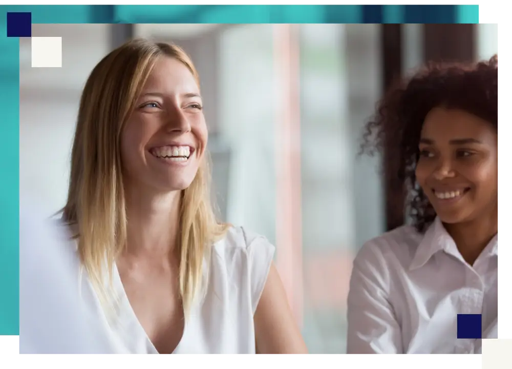 Two colleagues smiling during a relaxed conversation in a bright open-plan office